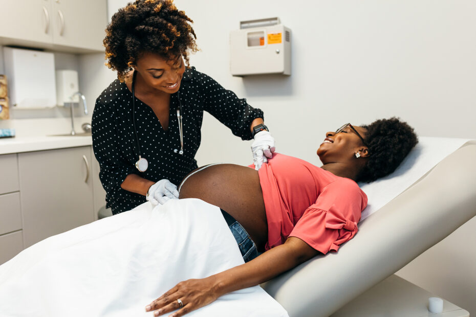 Black midwife feeling and measuring pregnant womans stomach for exam